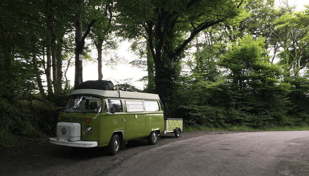 Green vintage van parked by forest road.