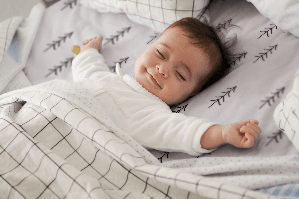 Smiling baby sleeping soundly in bed.