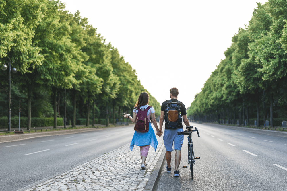 Couple walking, holding hands, trees lining road.