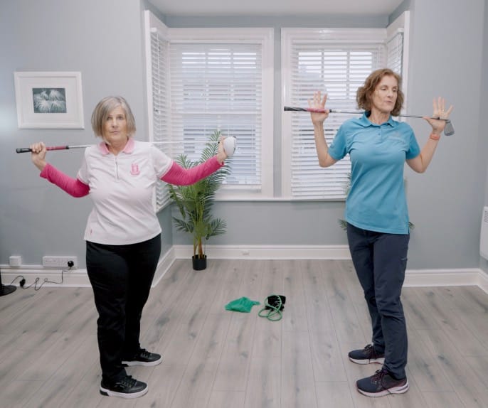 Two women exercising with golf clubs indoors